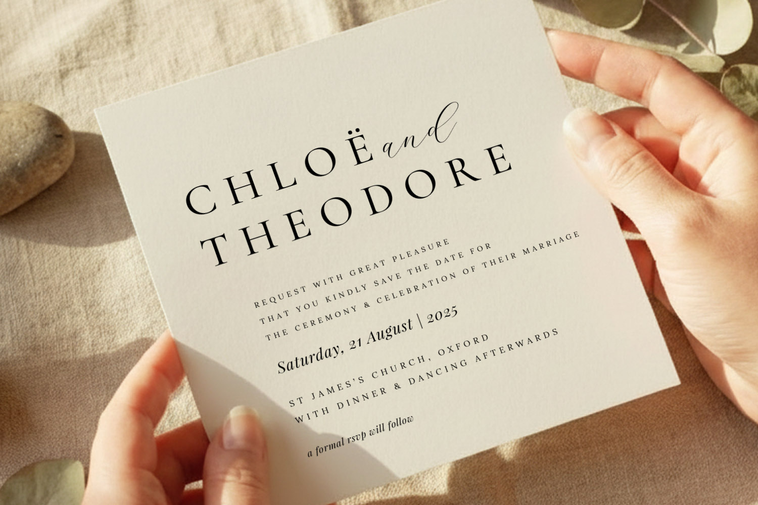 Wedding save the dates card in elegant cream with black modern calligraphy, held in hands on a neutral linen background.