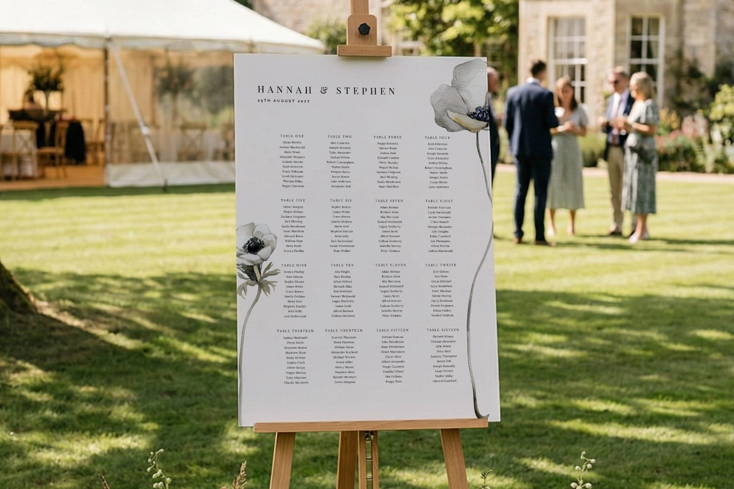 Wedding table plan with elegant black typography and floral accents displayed on an easel at an outdoor reception venue.