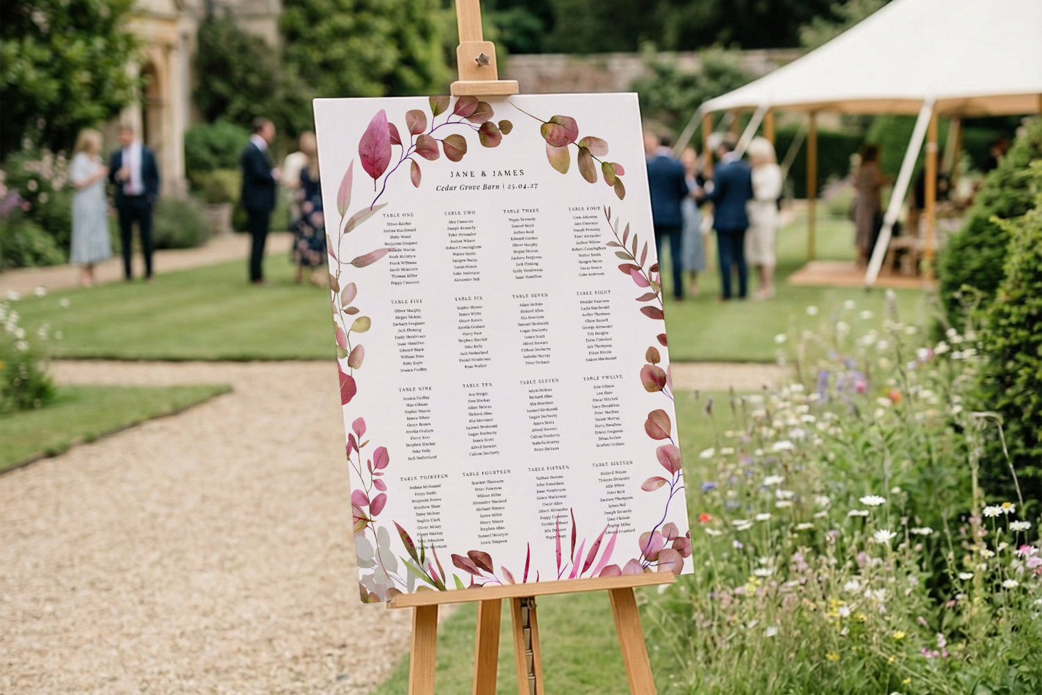 Wedding table plan with botanical border on an easel, displayed outdoors at a garden venue with guests in the background