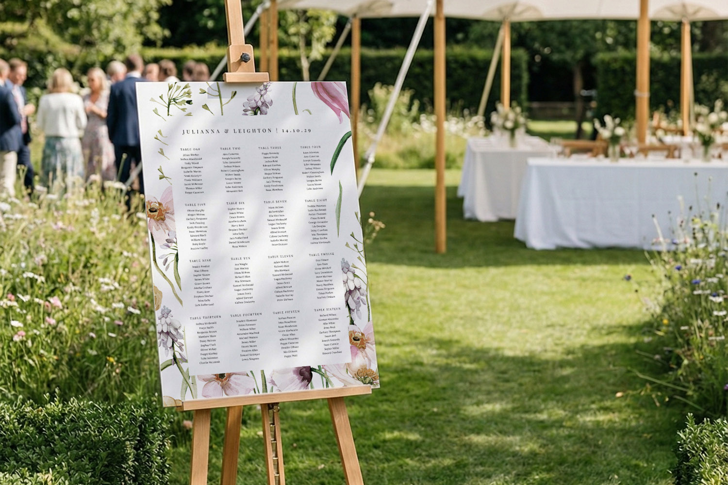 Wedding table plans with floral design displayed on an easel in a garden setting with tables and guests in the background.