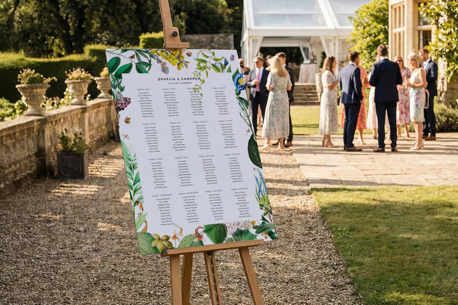 Wedding table plans with botanical border displayed on an easel outdoors at a garden venue with guests in the background