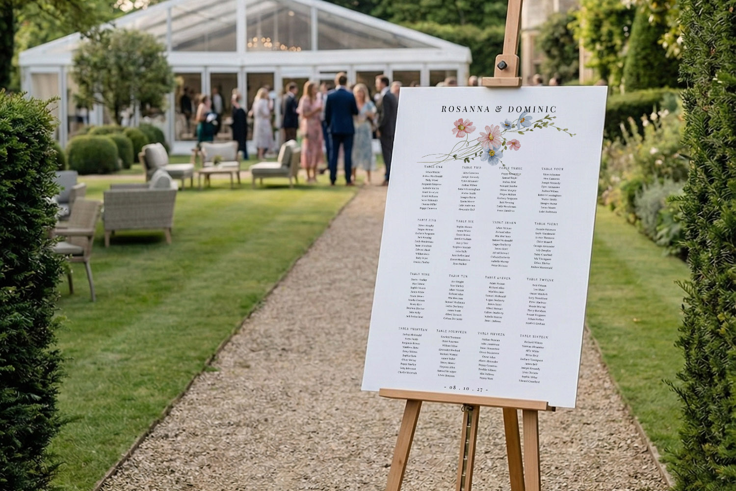 Wedding table plan displayed on an easel outdoors, featuring floral details and guest names, with a marquee in the