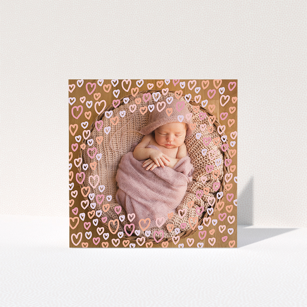 A baby thank you card design titled "Heart Overlay". It is a square (148mm x 148mm) card in a square orientation. It is a photographic baby thank you card with room for 1 photo. "Heart Overlay" is available as a folded card, with mainly pink colouring.