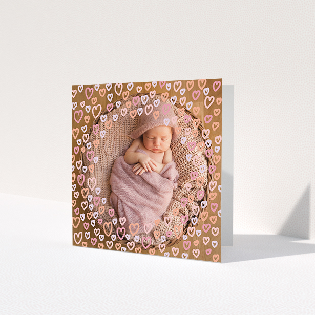 A baby thank you card design titled "Heart Overlay". It is a square (148mm x 148mm) card in a square orientation. It is a photographic baby thank you card with room for 1 photo. "Heart Overlay" is available as a folded card, with mainly pink colouring.
