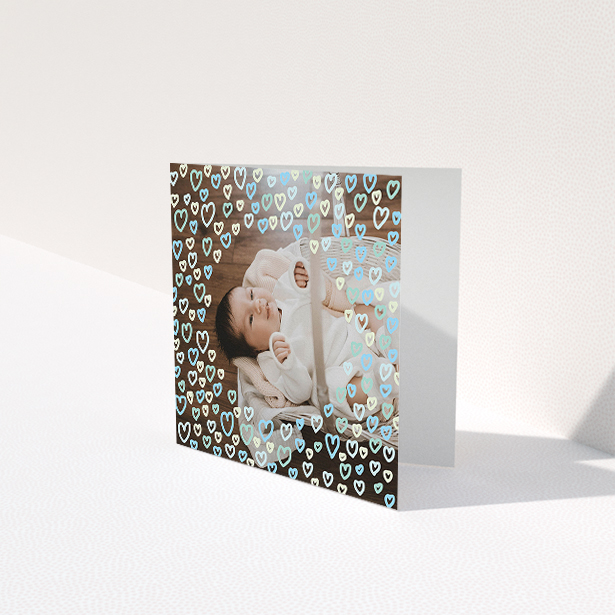 A baby thank you card named "Heart Overlay". It is a square (148mm x 148mm) card in a square orientation. It is a photographic baby thank you card with room for 1 photo. "Heart Overlay" is available as a folded card, with mainly blue colouring.