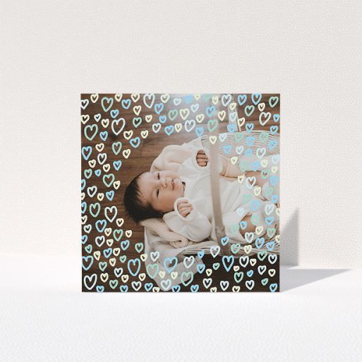 A baptism thank you card template titled "Blue Hearts". It is a square (148mm x 148mm) card in a square orientation. It is a photographic baptism thank you card with room for 1 photo. "Blue Hearts" is available as a folded card, with tones of blue, light blue and green.