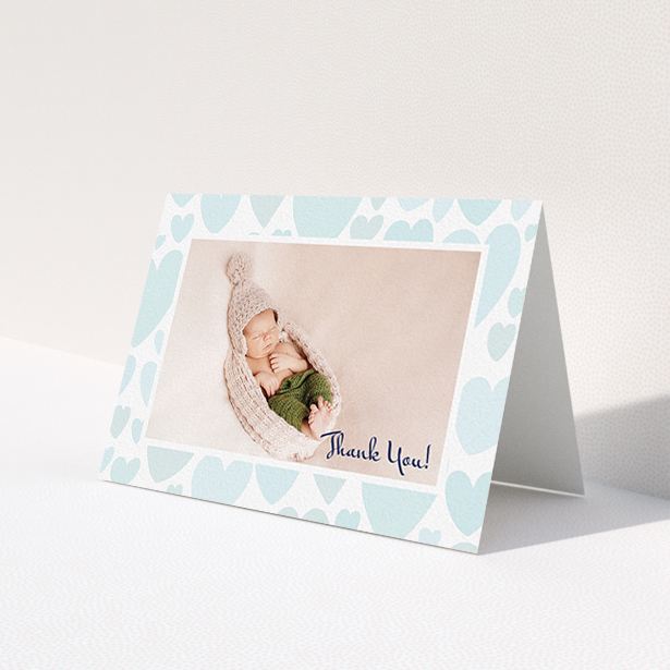 A baptism thank you card named 'Pastel Hearts'. It is an A6 card in a landscape orientation. It is a photographic baptism thank you card with room for 1 photo. 'Pastel Hearts' is available as a folded card, with tones of blue and white.