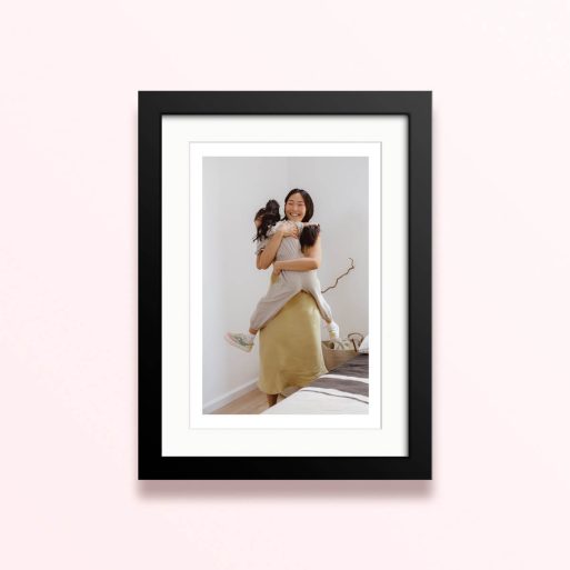 Framed and mounted photo print with one photo of a woman hugging a child in a bright room.