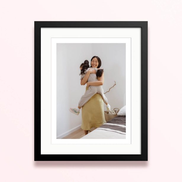 Framed and mounted photo print with one photo of a woman hugging a child in a bright room.