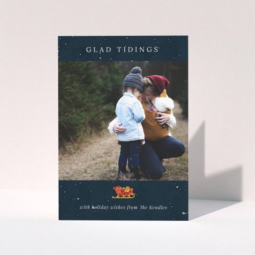 A custom christmas card design called "Glad Tidings with Sleigh". It is an A5 card in a portrait orientation. It is a photographic custom christmas card with room for 1 photo. "Glad Tidings with Sleigh" is available as a folded card, with tones of blue and white.