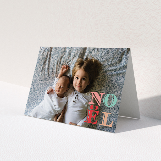 A custom christmas card design named "Pastel Noel". It is an A5 card in a landscape orientation. It is a photographic custom christmas card with room for 1 photo. "Pastel Noel" is available as a folded card, with mainly pink colouring.