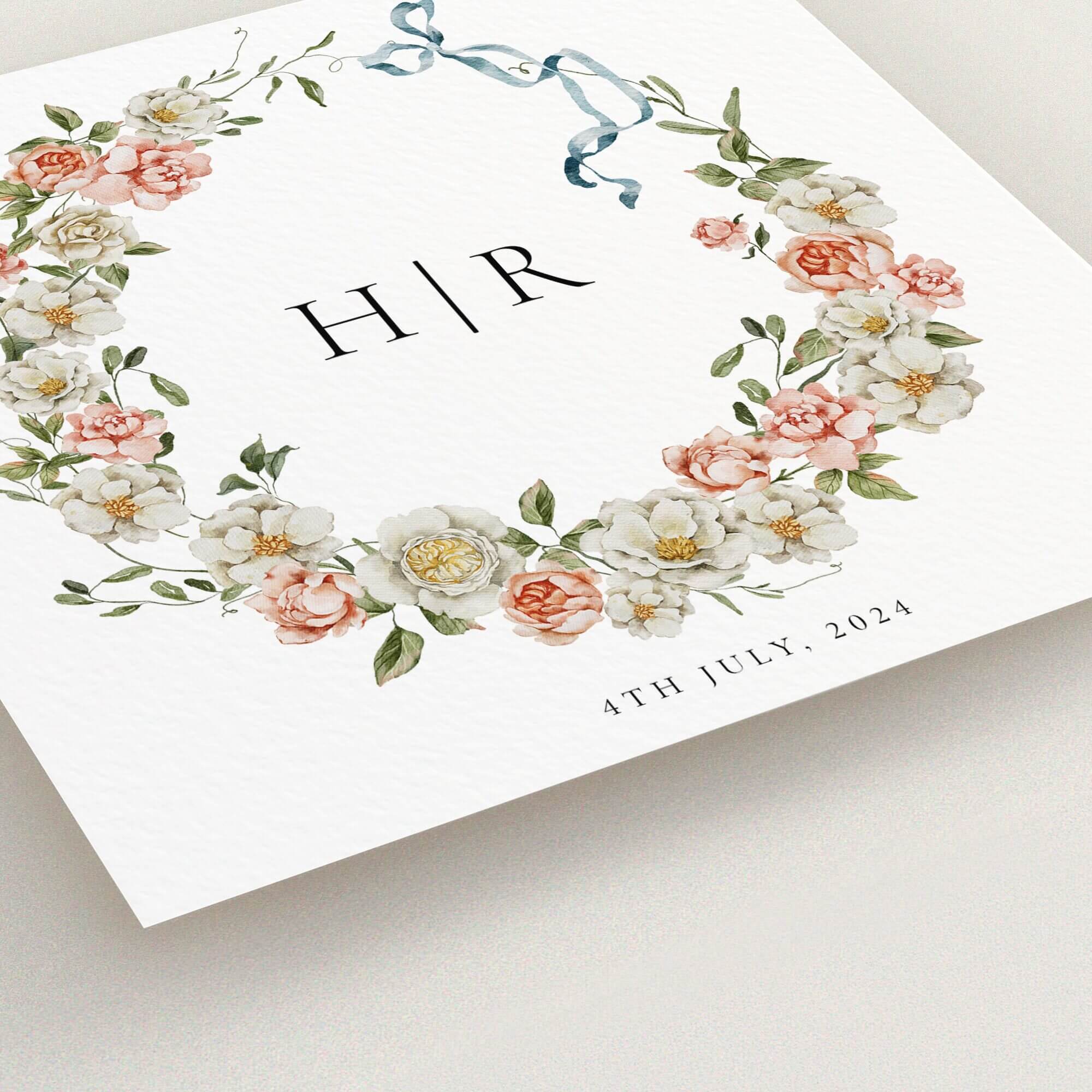 Floral wreath wedding invitation design with monogram and blue ribbon, no photos included.