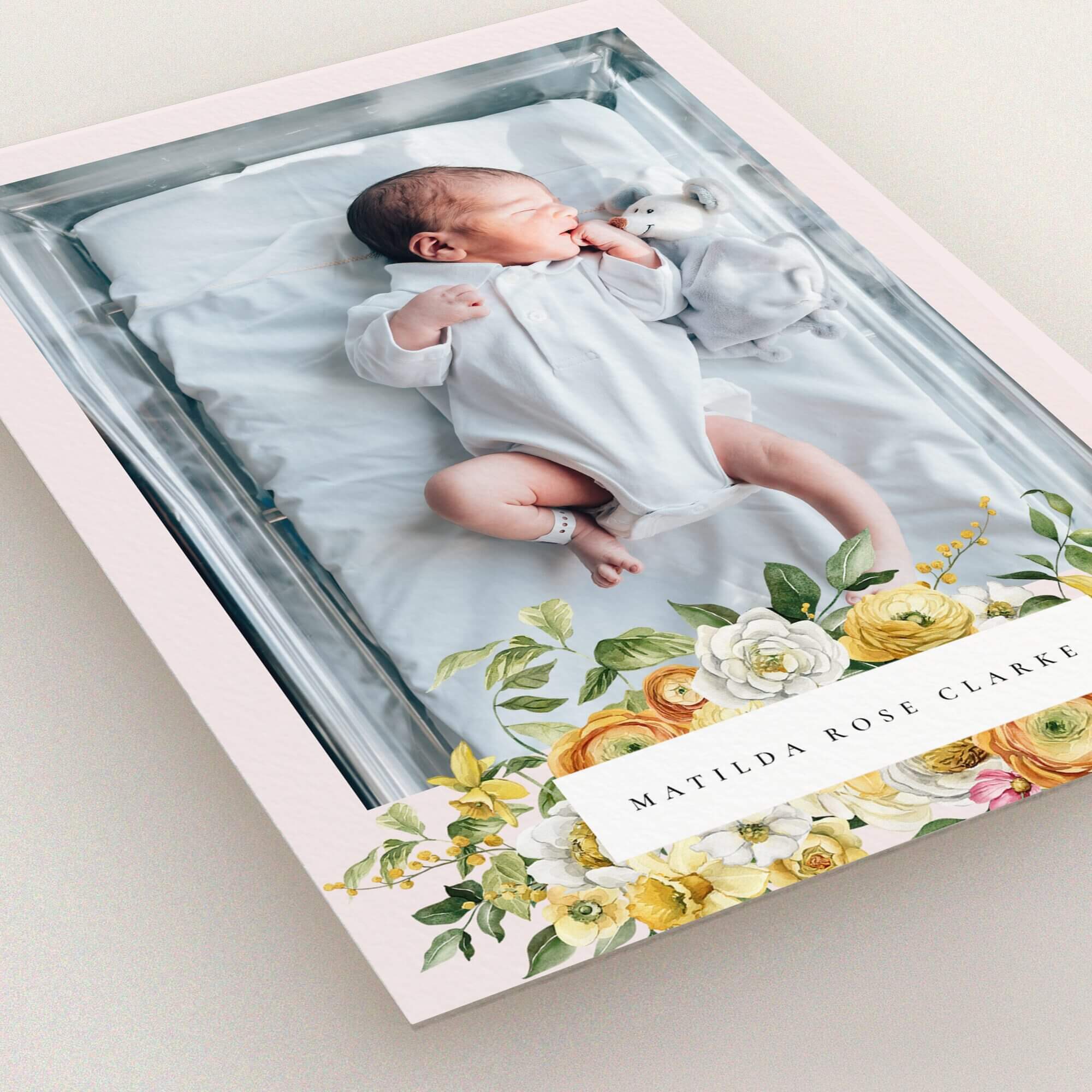 Floral design birth announcement card with a baby photo in a crib and colourful flowers.