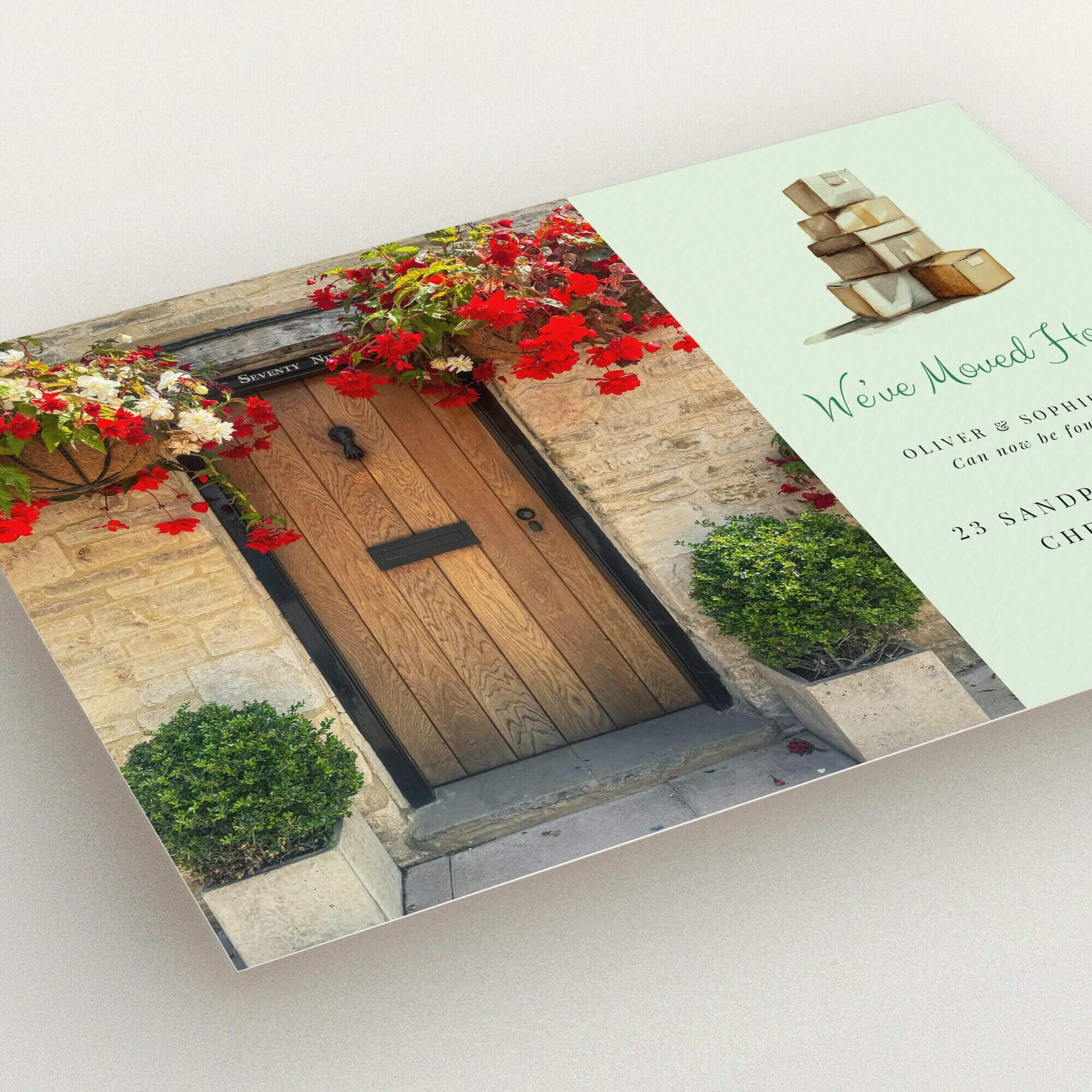 Change of address card with a front door and floral decorations on the left and stacked moving boxes illustration on the right.