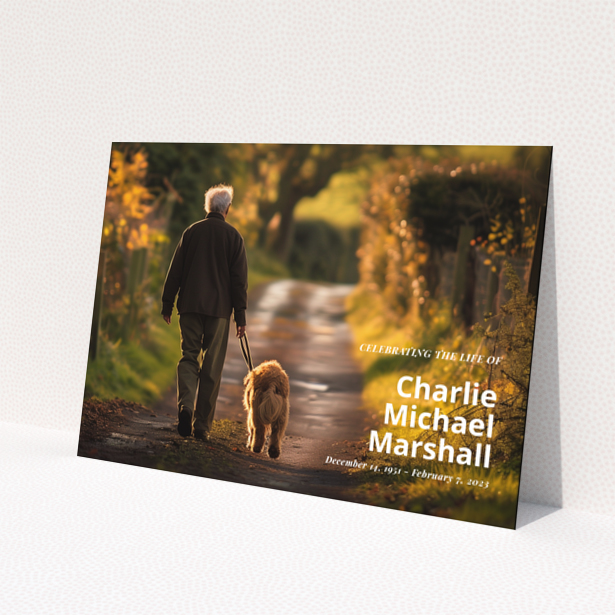 Funeral announcement card with a photo of a man walking a dog along a path with autumn foliage.