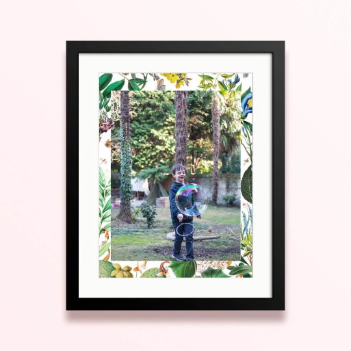 Framed and mounted photo print with floral border and one photo of a child playing with a bubble in a lush garden setting.