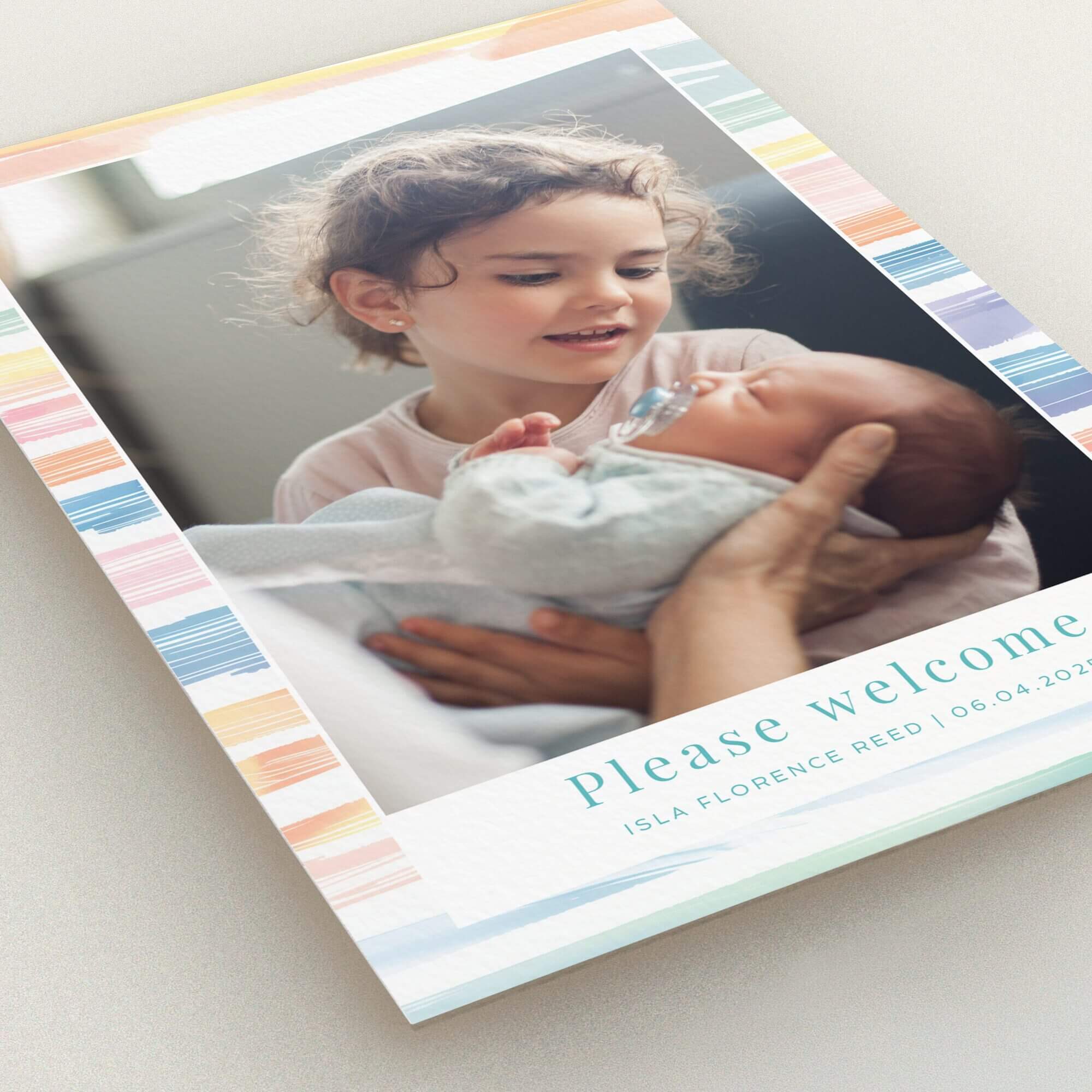 Colourful birth announcement card featuring a photo of a child holding a baby.