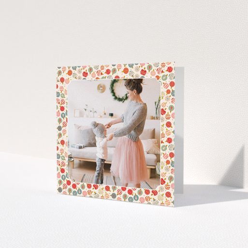 A personalised christmas card called 'Bauble Photo'. It is a square (148mm x 148mm) card in a square orientation. It is a photographic personalised christmas card with room for 1 photo. 'Bauble Photo' is available as a folded card, with tones of pink, red and light blue.