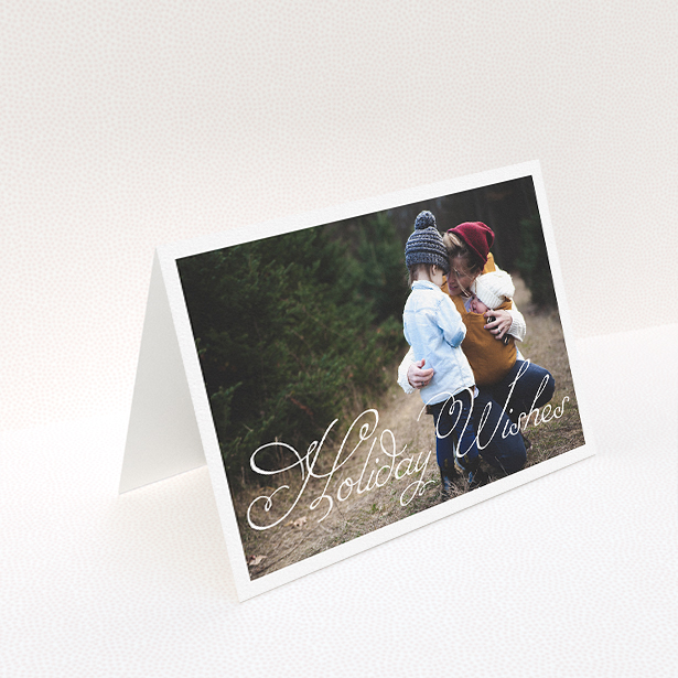 A personalised christmas card called "Holiday Wishes". It is an A5 card in a landscape orientation. It is a photographic personalised christmas card with room for 1 photo. "Holiday Wishes" is available as a folded card, with mainly white colouring.