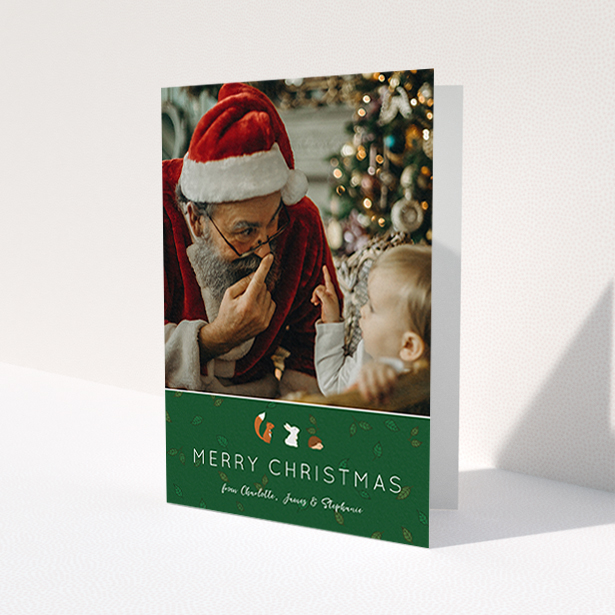 A personalised christmas card design named 'Woodland Christmas'. It is an A6 card in a portrait orientation. It is a photographic personalised christmas card with room for 1 photo. 'Woodland Christmas' is available as a folded card, with tones of green and white.
