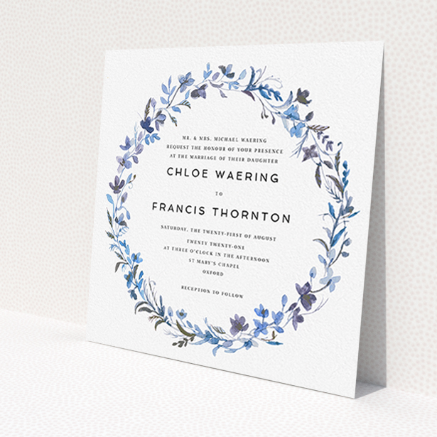 A personalised wedding invite design titled "Blue Floral Wreath". It is a square (148mm x 148mm) invite in a square orientation. "Blue Floral Wreath" is available as a flat invite, with tones of light blue, purple and grey.