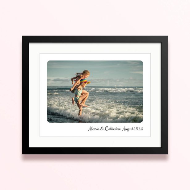 Framed and mounted photo print featuring a beach scene with two children playing in the waves.