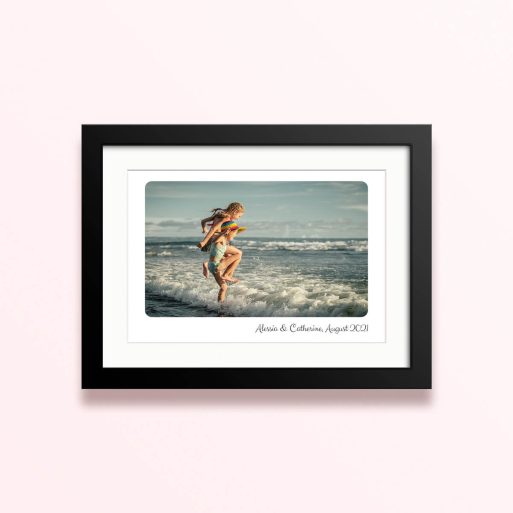 Framed and mounted photo print featuring a beach scene with two children playing in the waves.