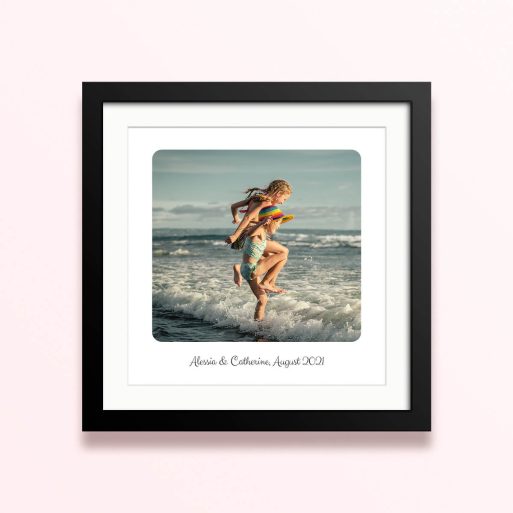 Framed and mounted photo print featuring a beach scene with two children playing in the waves.