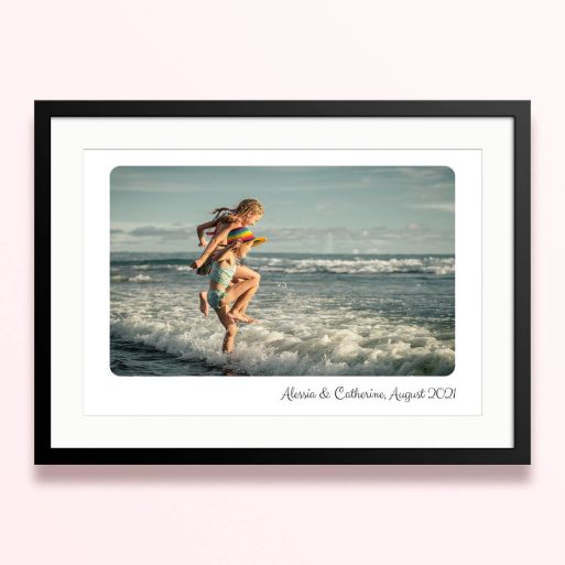 Framed and mounted photo print featuring a beach scene with two children playing in the waves.