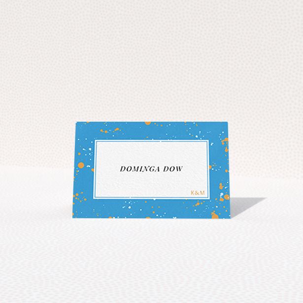 A table place card named "Orange Splatters". It is an 85 x 55mm card in a landscape orientation. "Orange Splatters" is available as a folded card, with tones of light blue and orange.