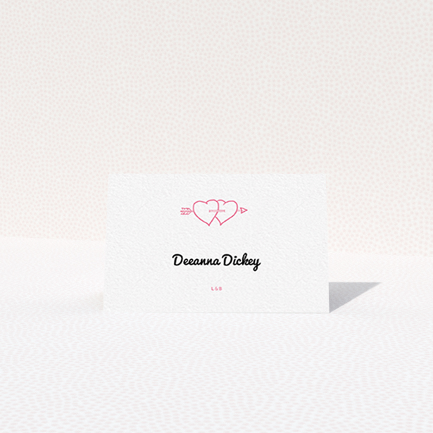 A table place card named "Shot to the Hearts". It is an 85 x 55mm card in a landscape orientation. "Shot to the Hearts" is available as a folded card, with tones of white and pink.
