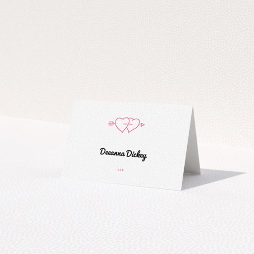 A table place card named 'Shot to the Hearts'. It is an 85 x 55mm card in a landscape orientation. 'Shot to the Hearts' is available as a folded card, with tones of white and pink.