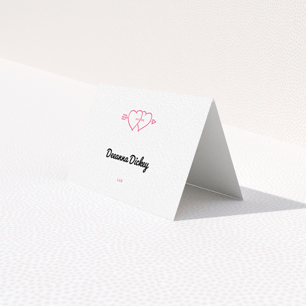 A table place card named "Shot to the Hearts". It is an 85 x 55mm card in a landscape orientation. "Shot to the Hearts" is available as a folded card, with tones of white and pink.