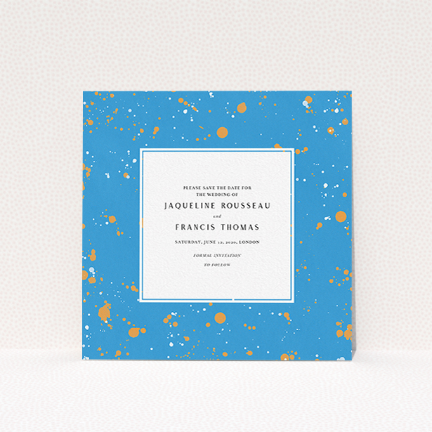 A wedding save the date card called "Orange Splatters". It is a square (148mm x 148mm) card in a square orientation. "Orange Splatters" is available as a flat card, with tones of light blue and orange.