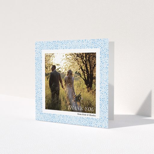 A wedding thank you card design called 'Surrounded by flowers'. It is a square (148mm x 148mm) card in a square orientation. It is a photographic wedding thank you card with room for 1 photo. 'Surrounded by flowers' is available as a folded card, with tones of blue and white.